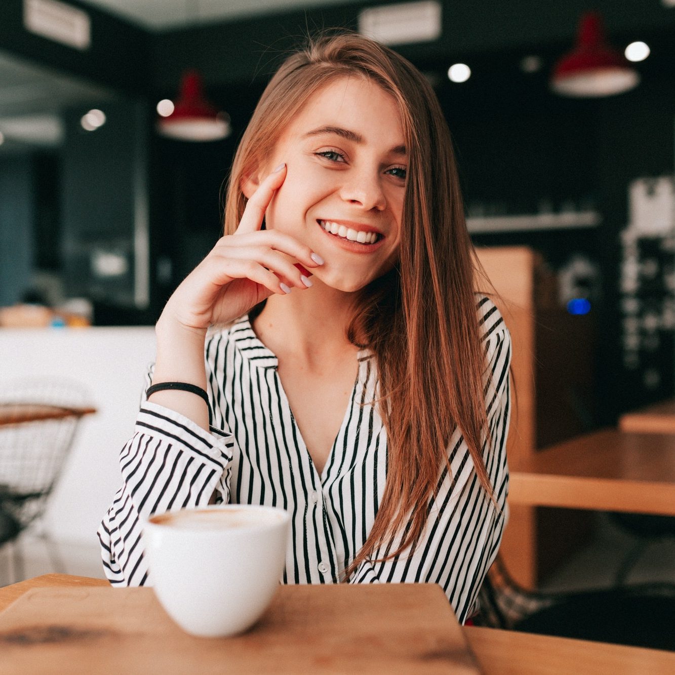 adorable charming lady with long hair wearing trendy blouse sitting in cafeteria with great smile