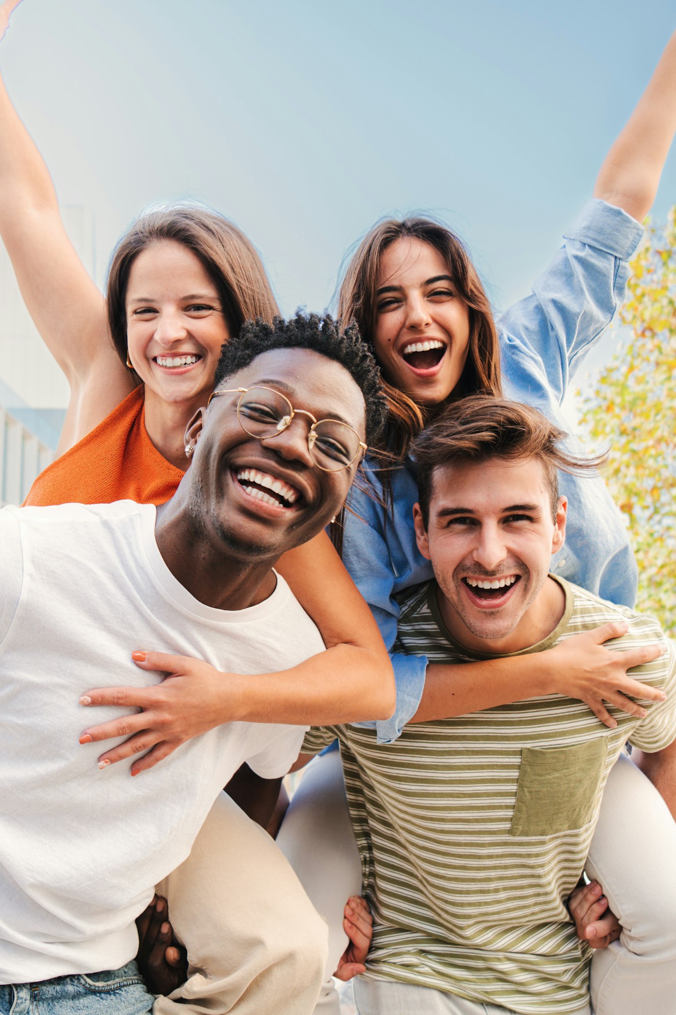 Vertical portrait of two multiracial young friends giving piggyback ride to his girlfriends. A group