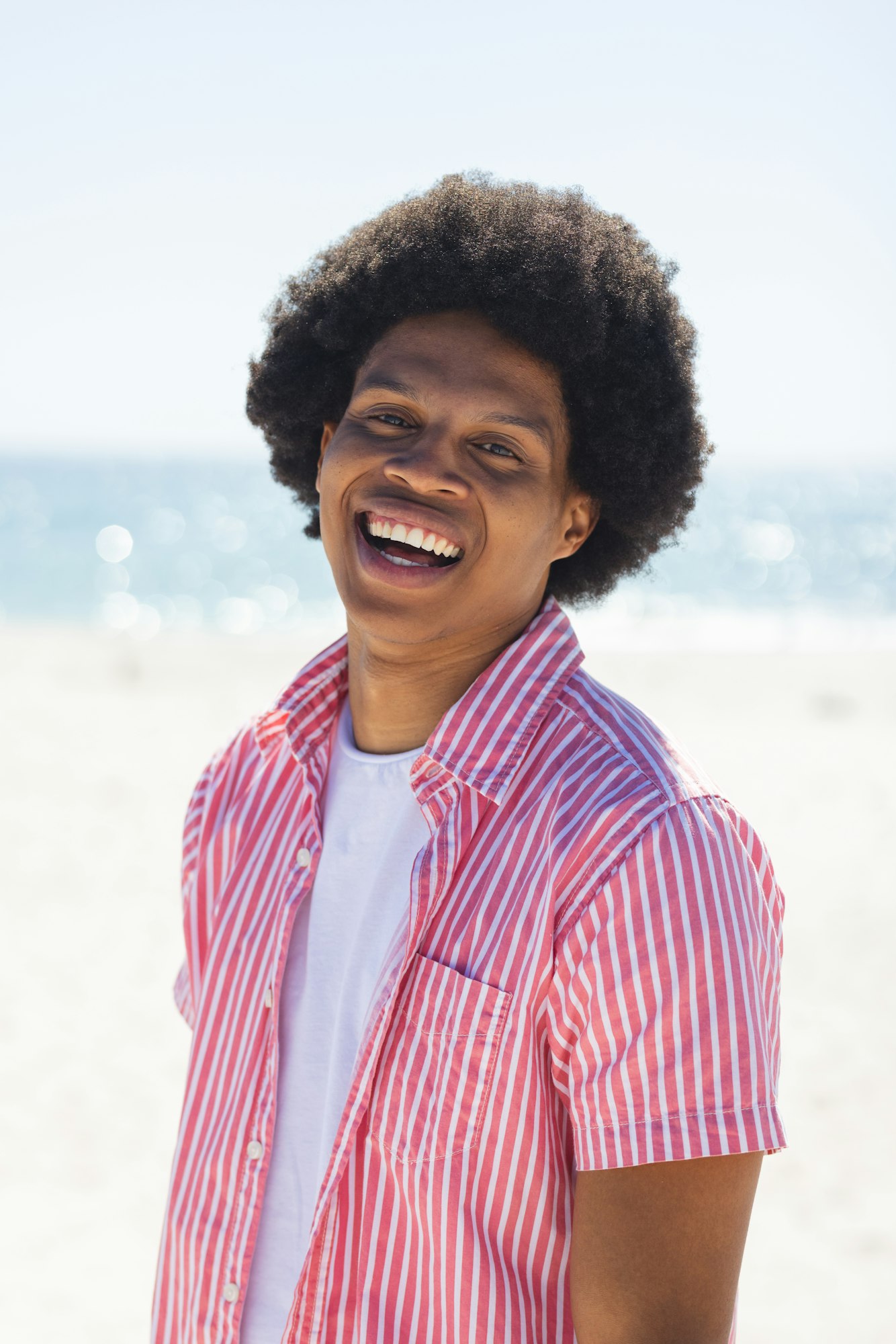 A young African American man smiles brightly outdoors at the beach