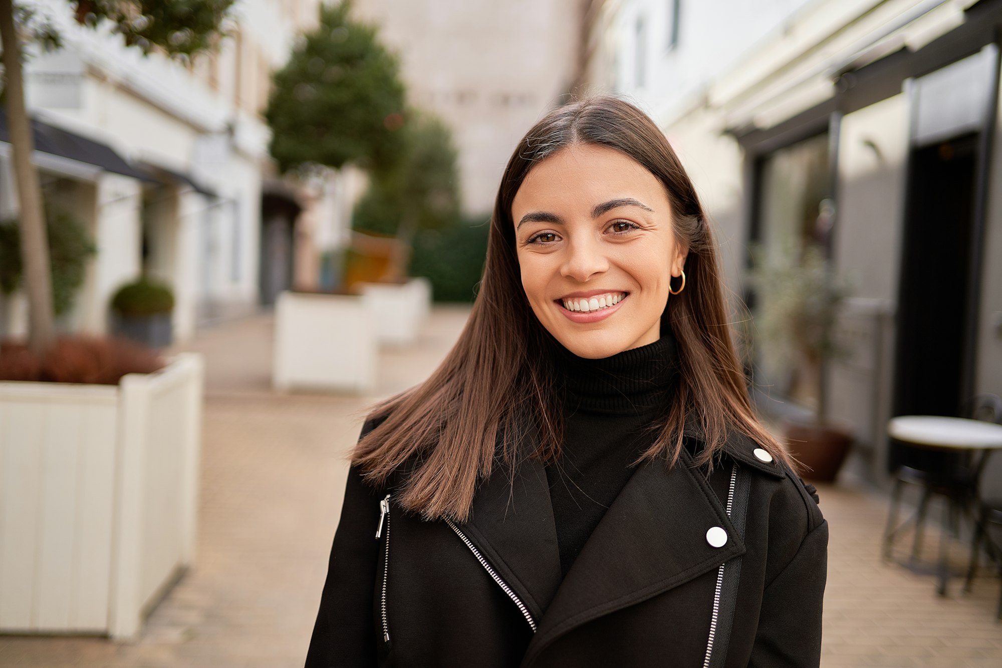 Close-up of a stylish woman smiling while standing outdoors.