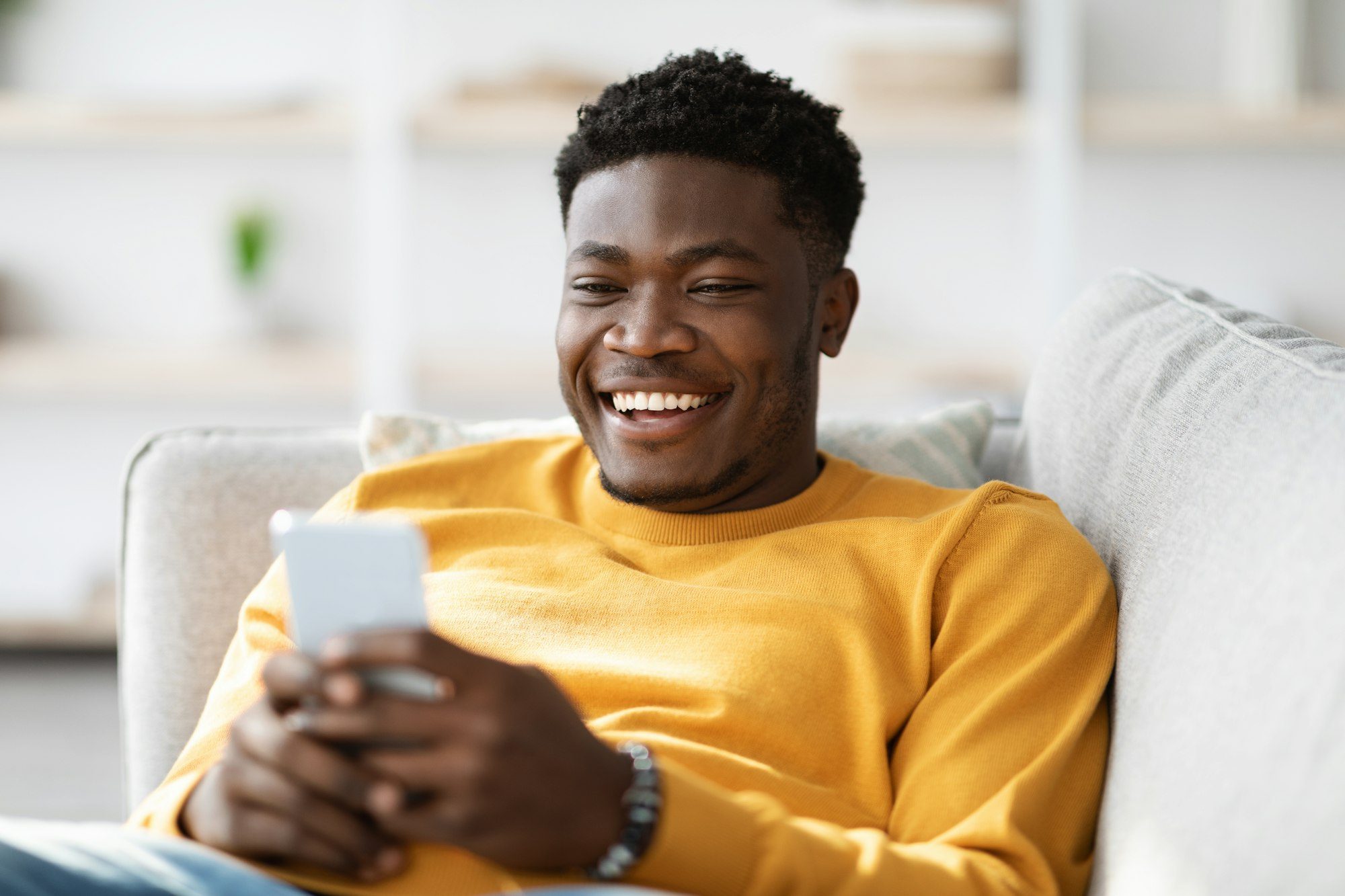 Smiling african american man reclining on couch with cellphone