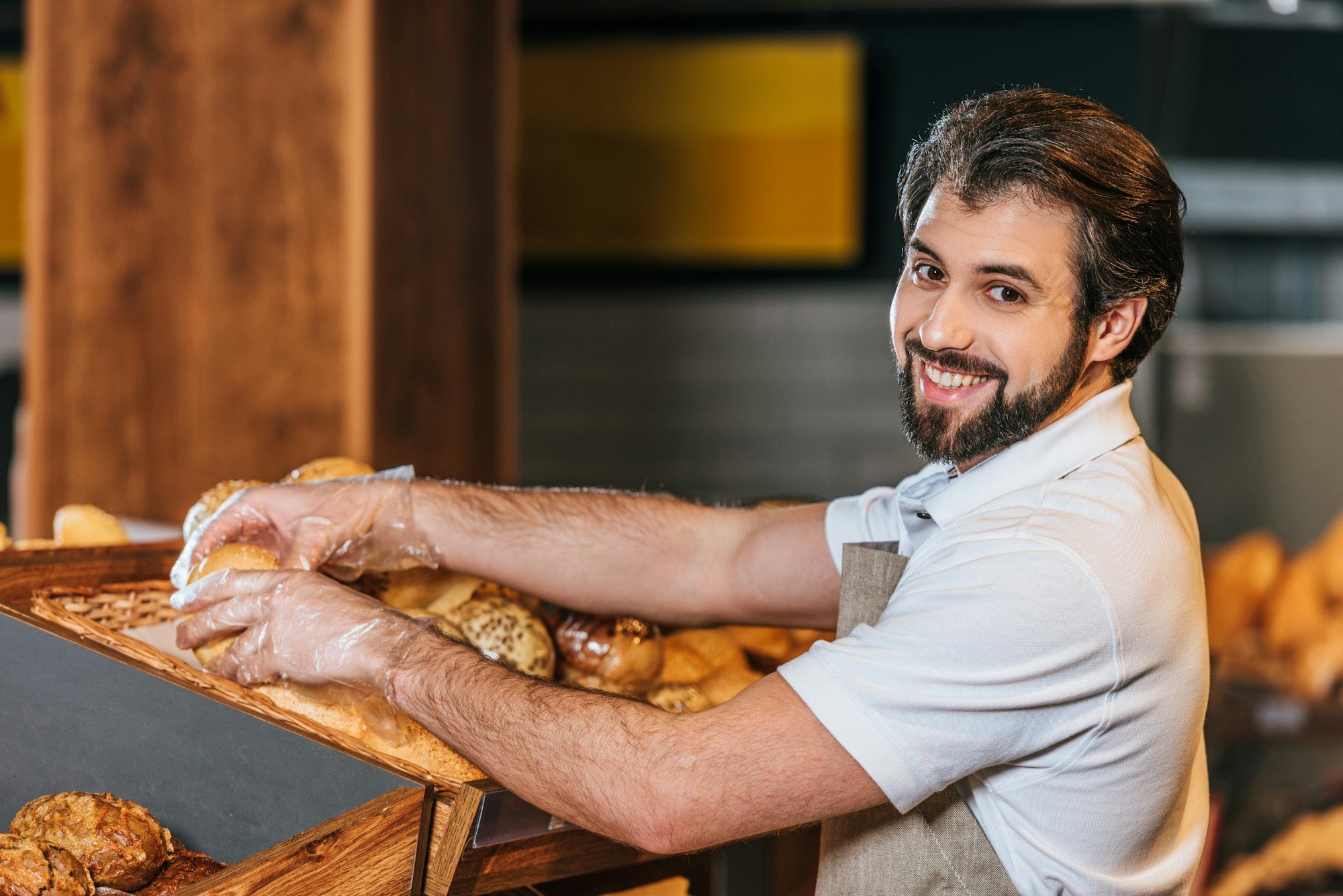 smiling male shop assistant arranging fresh pastry in supermarket