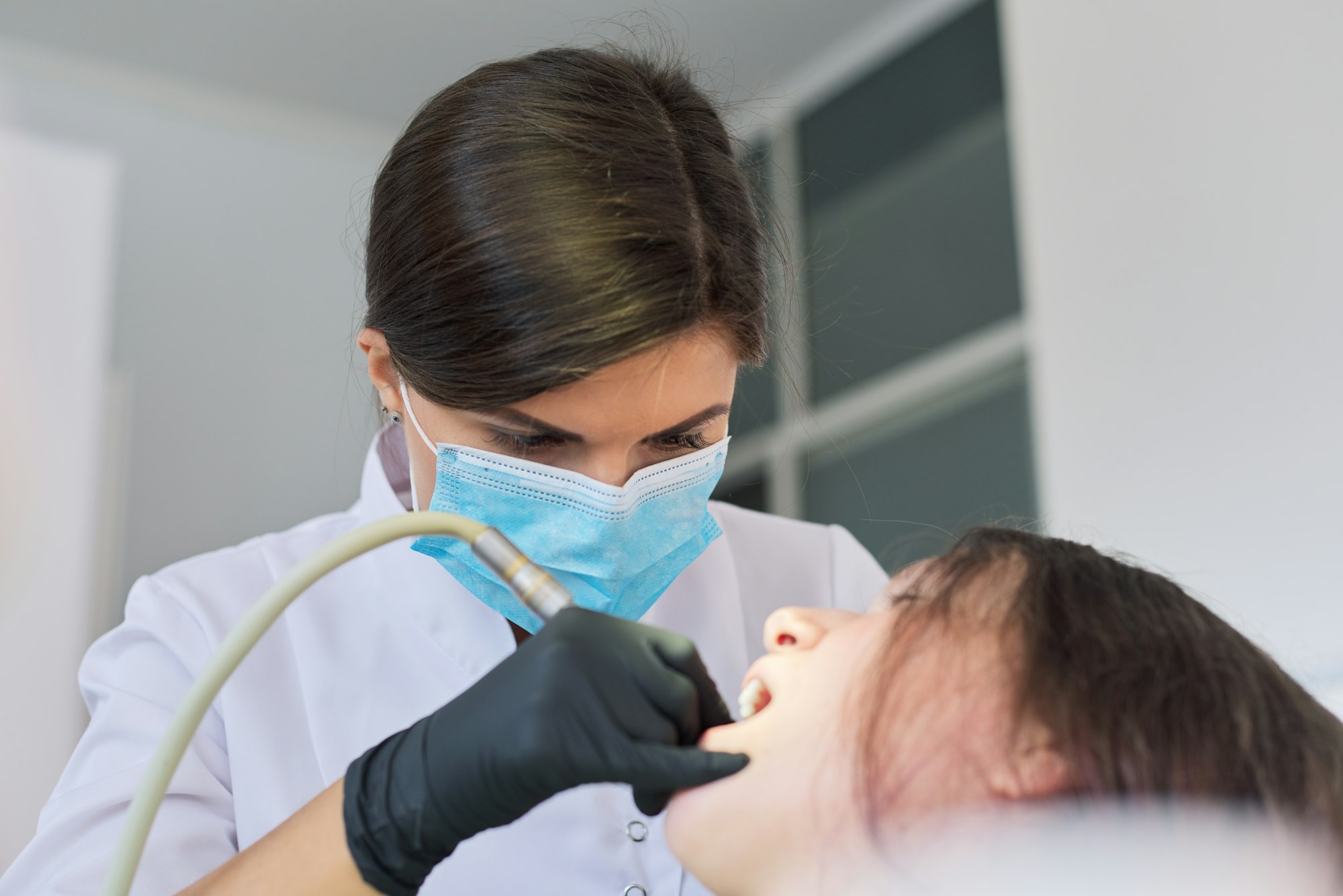 Woman dentist treating teeth to a patient sitting in dental chair using professional equipment