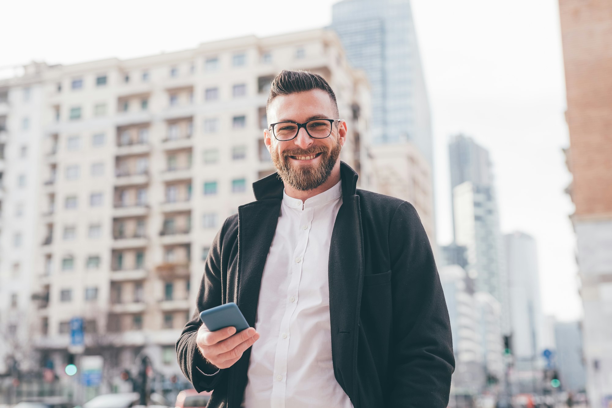 Young bearded caucasian man holding smartphone smiling happy and postive having fun