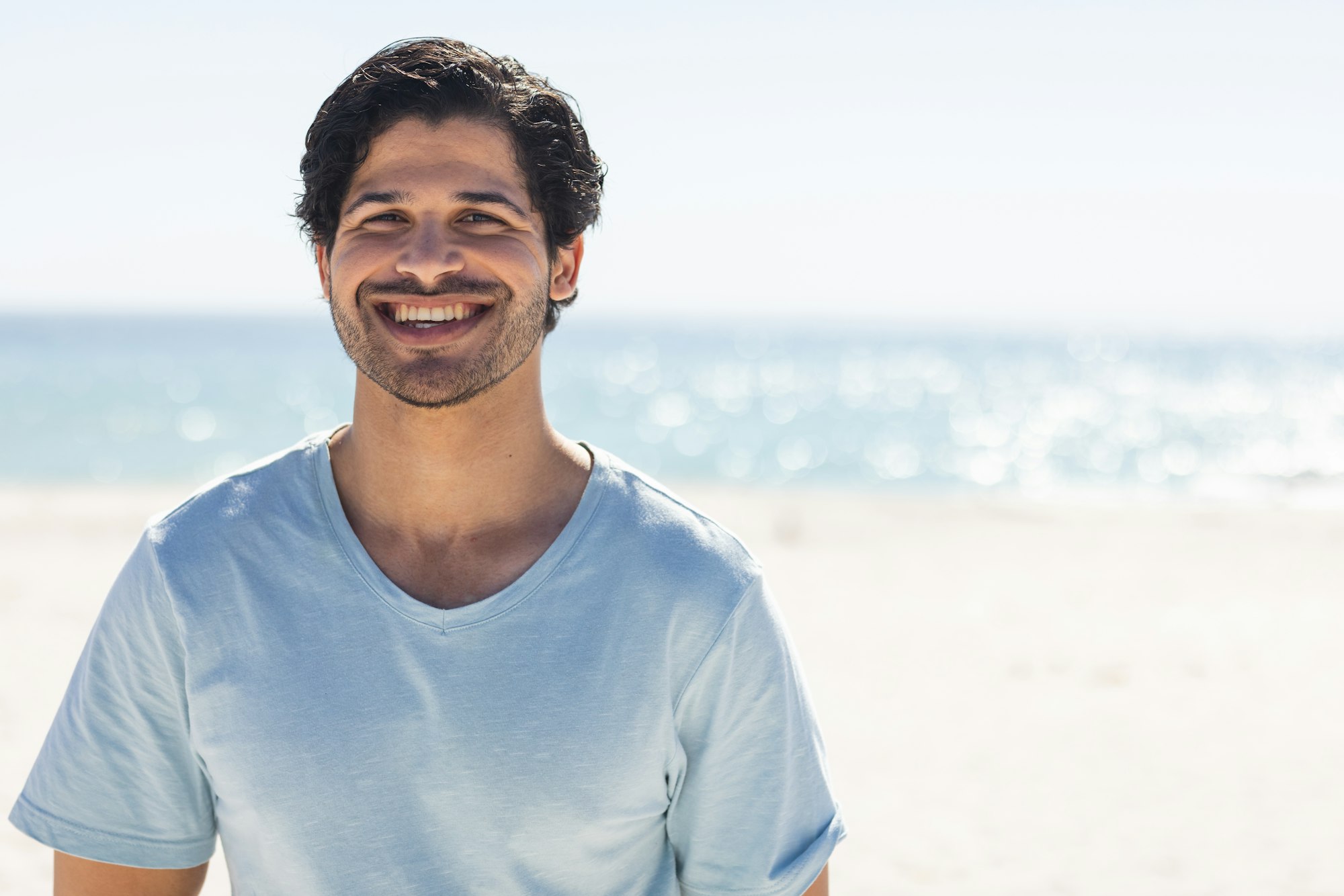 Young biracial man smiles brightly at the beach